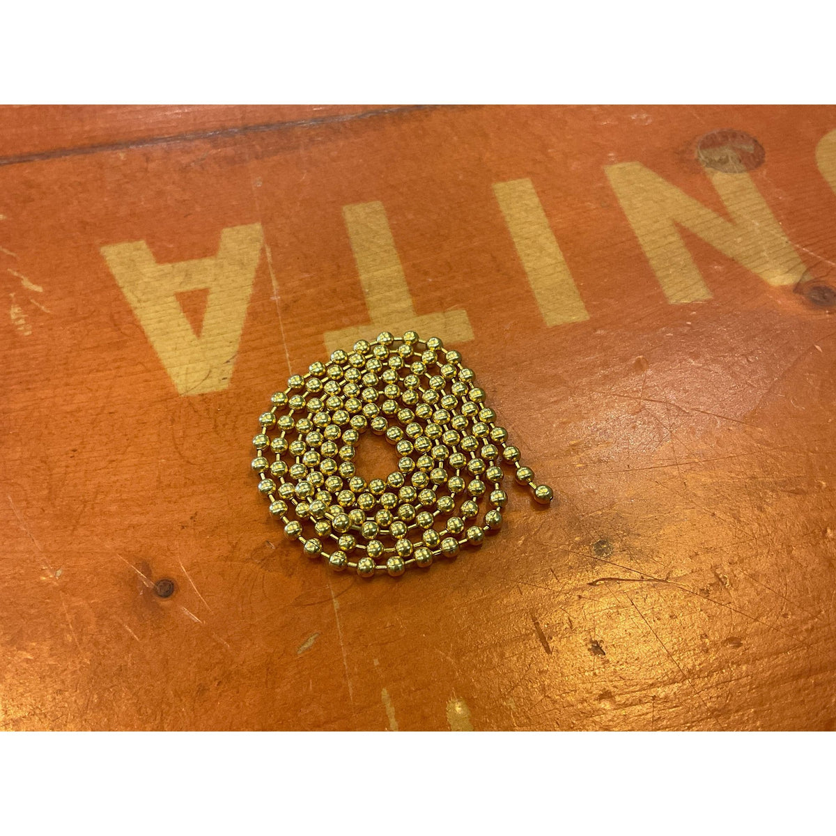 Small gold bead chain for fly tying, coiled on wood