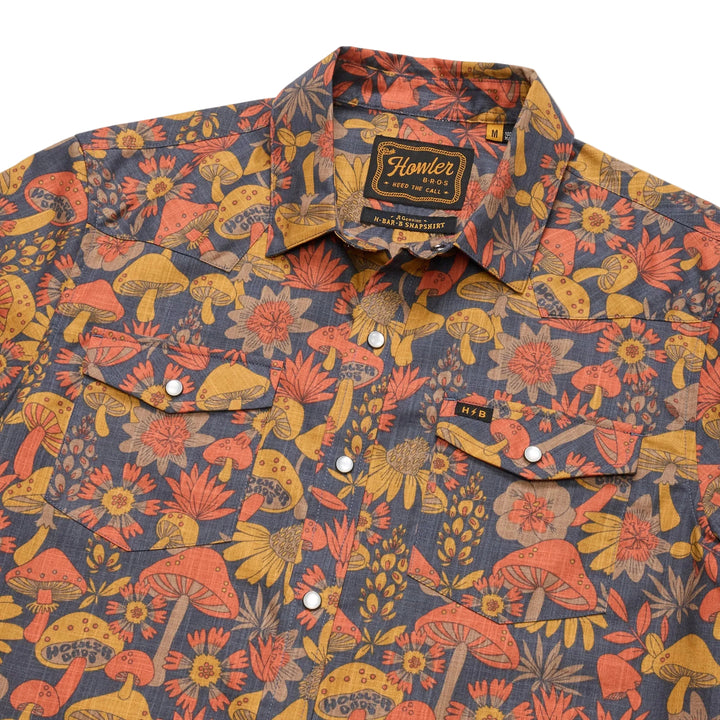 Close-up of navy Howler Bros snapshirt collar, pearl snaps, and chest pockets with vintage mushroom pattern
