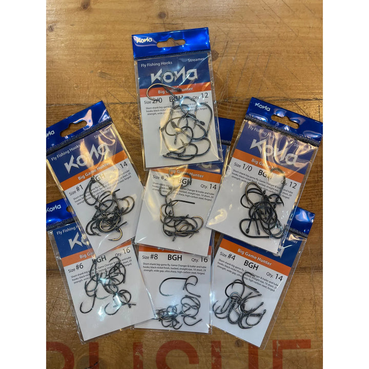 Assorted sizes of Kona Big Game Hunter fly fishing hooks on wooden table