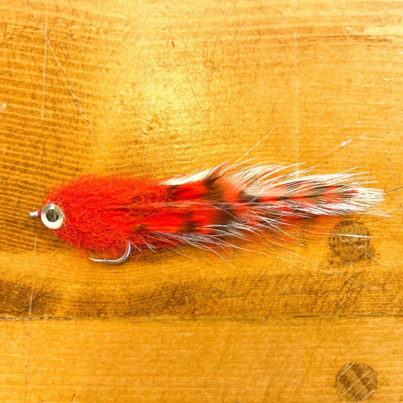 Red and white Mini Brush Fly fishing lure with oversized Living Eye on wooden surface