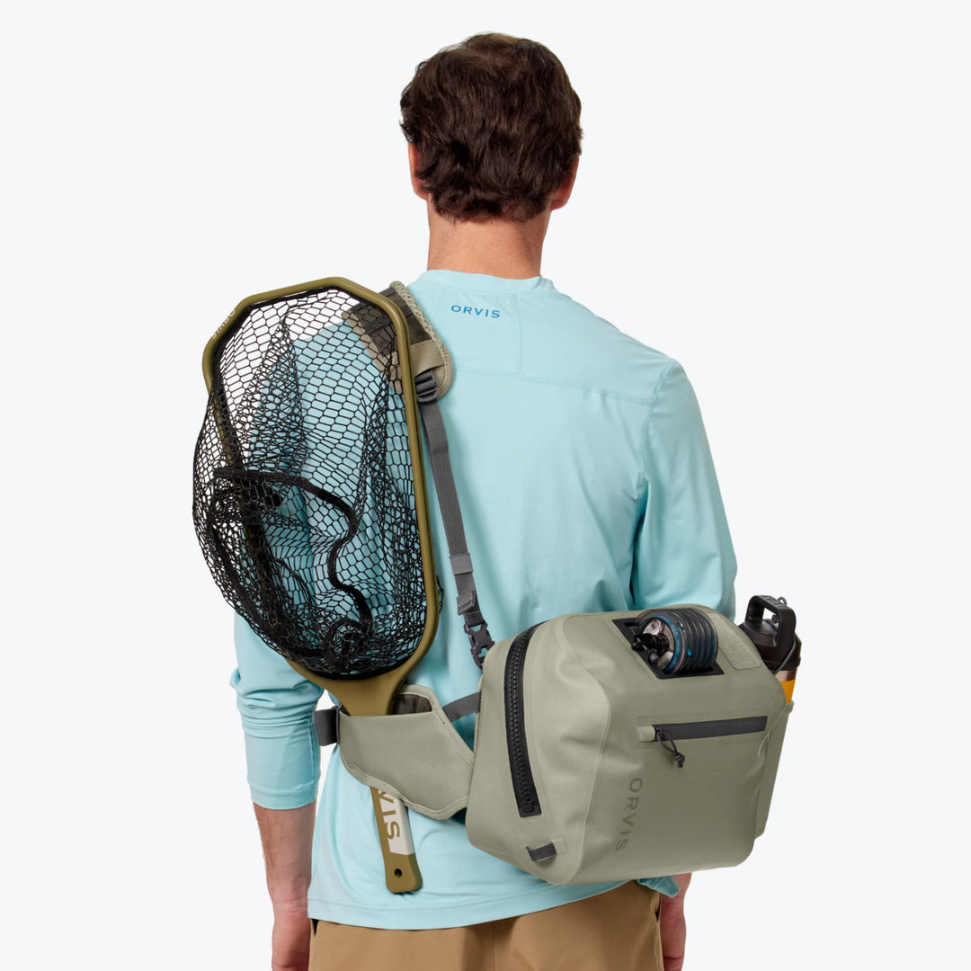 Angler wearing sage green Orvis PRO waterproof hip pack with fishing net and line spool attached