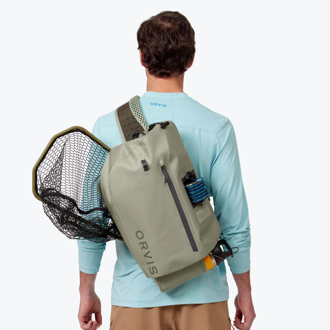 Angler wearing Orvis PRO Waterproof Sling Pack with attached net and water bottle