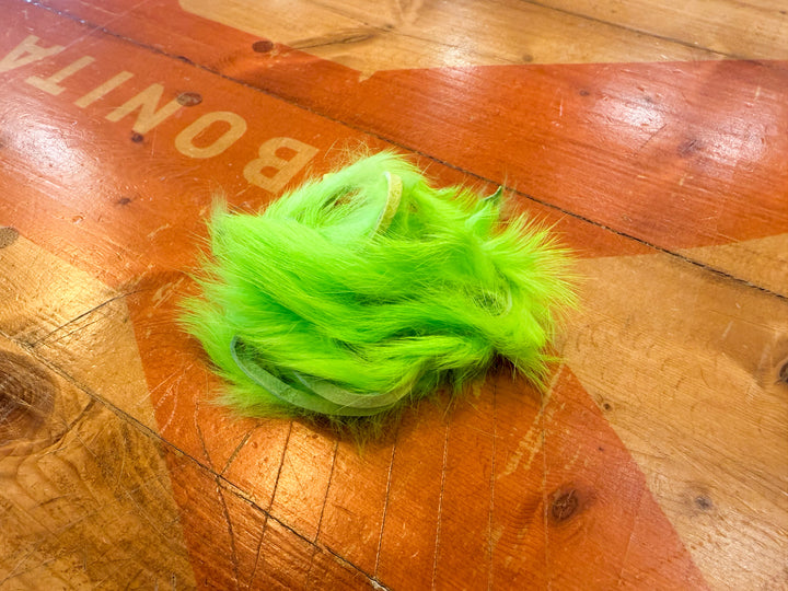 Neon green rabbit fur strips for fly tying on wooden surface