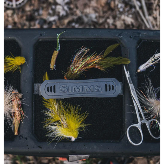 Close-up of Simms branded fly box organizer tray with colorful flies and forceps