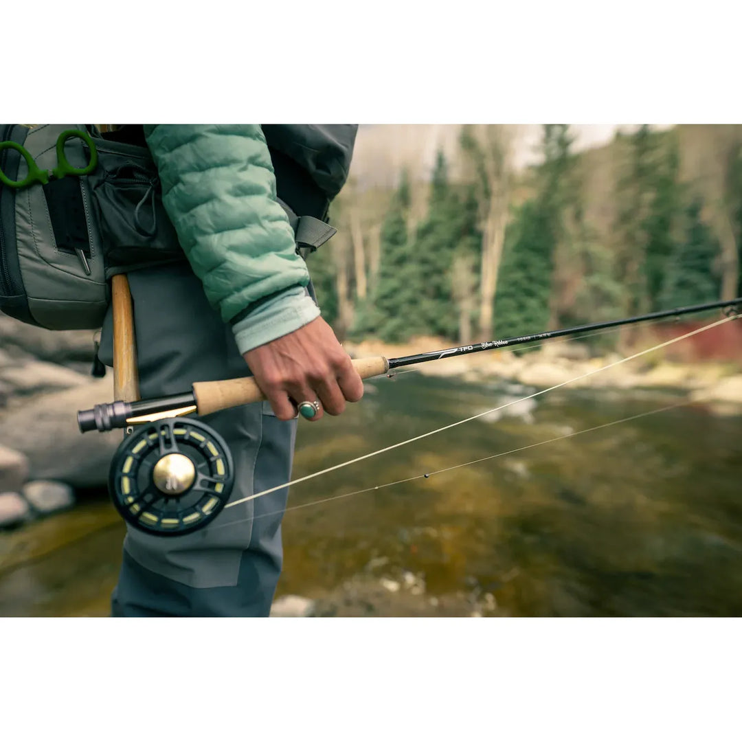 Angler gripping TFO Blue Ribbon fly rod cork handle with reel on river bank