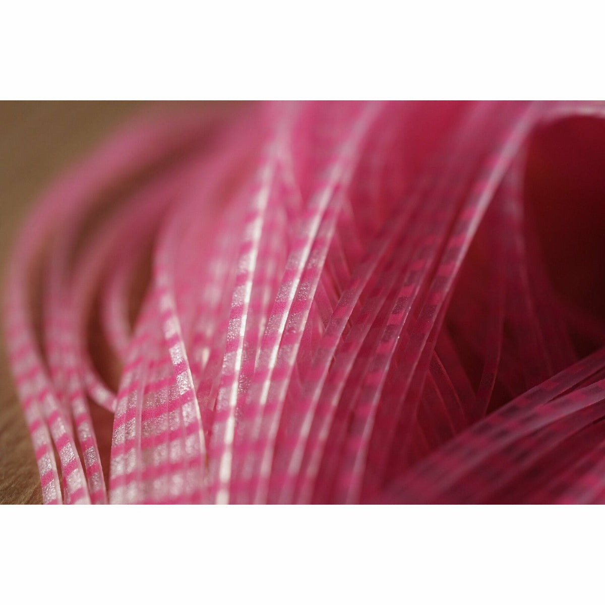 Close-up of pink barred clear Crusher Legs fly tying material showing translucent strands with opaque pink bars