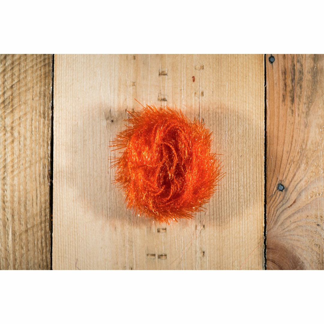 Hot orange synthetic hackle fly tying material with glitter flash on wood