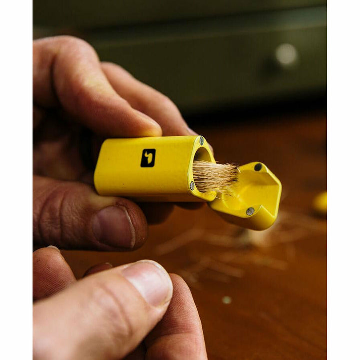 Hands using open yellow hair stacker to align brown fibers for fly tying