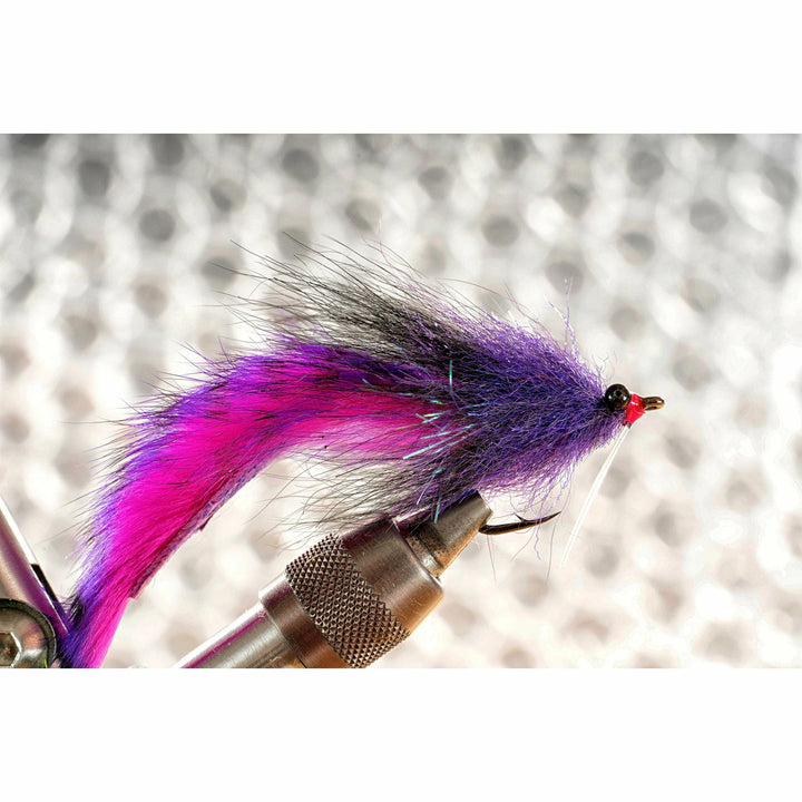 Close-up of finished neon grape Megalolipop fly in tying vise showing purple fiber body and magenta tail