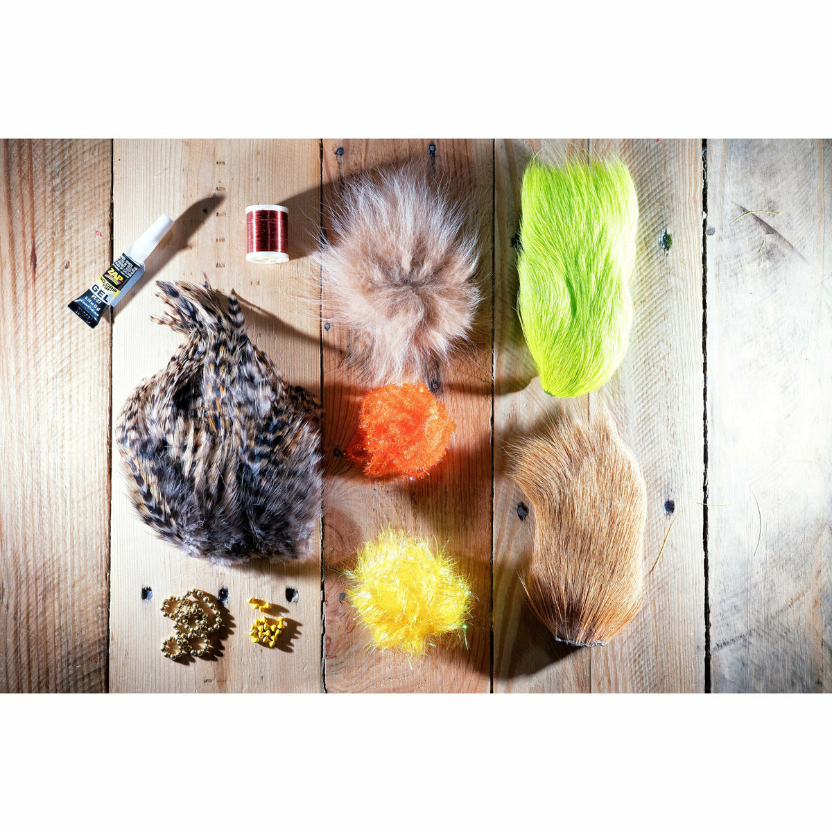 Redfish Crouton DIY Fly Tying Kit materials: chartreuse and tan chenille, deer belly hair, fox hair, thread, eyes, and bead chain on wood