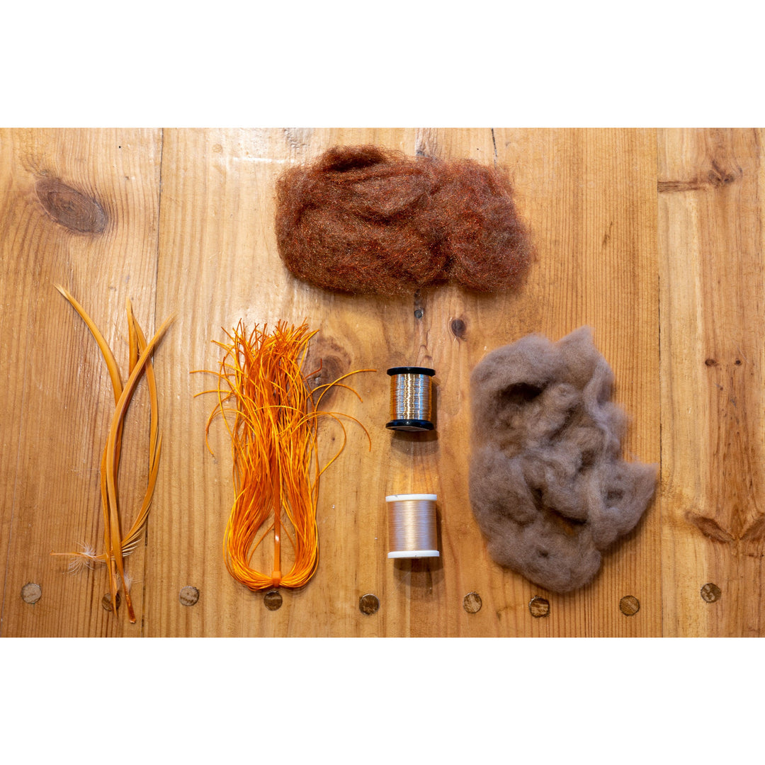 Fly tying kit materials including gold biots, orange floss, thread spools, and dubbing